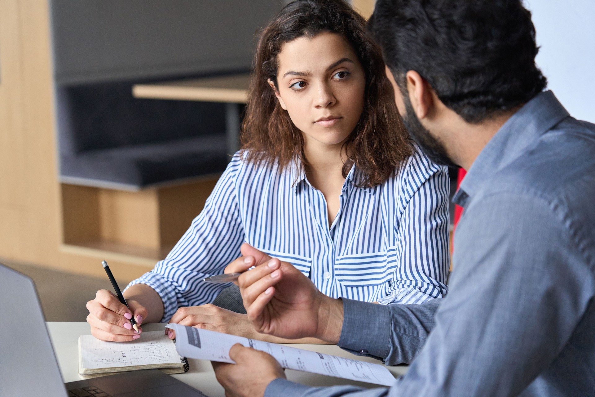 Mentoring young male Hispanic teacher and latin indian female student working together discussing course work. Insurance agent manager explaining conditions to client.