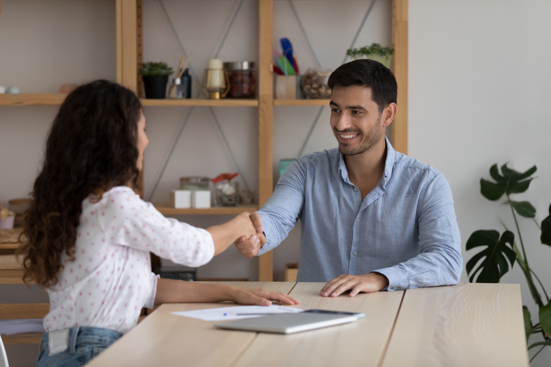 Businesspeople handshake after negotiations, seated at desk in company office